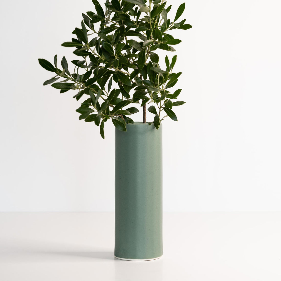 Modern cylinder porcelain vase in soft green and white standing on a white surface.