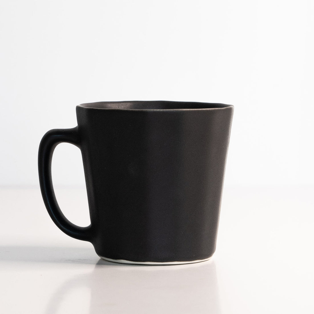 Matte black handmade porcelain coffee mug with an ergonomic oval handle design.
