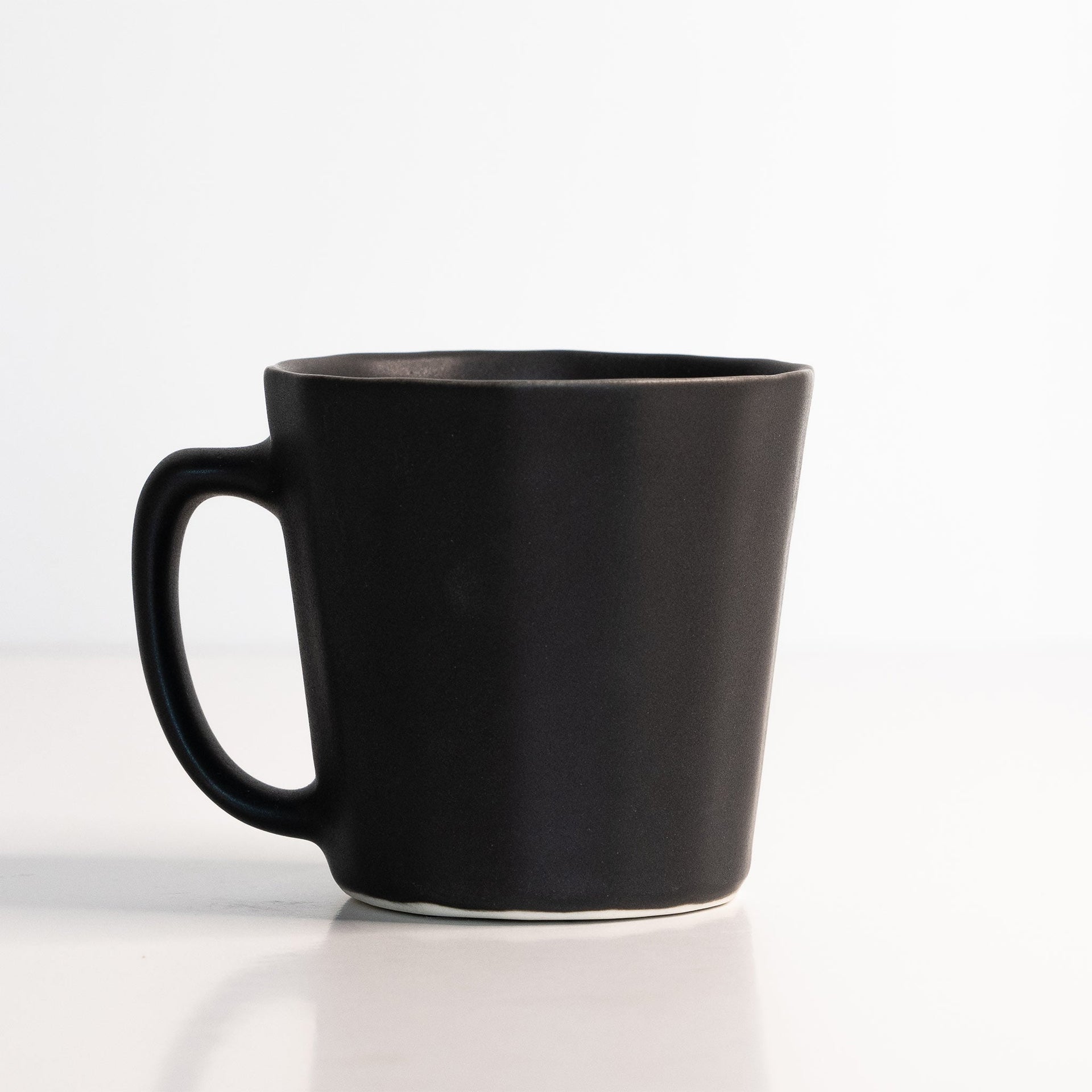 Matte black handmade porcelain coffee mug with an ergonomic oval handle design.