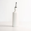 White porcelain olive oil dispenser bottle with a stainless steel pouring spout on a neutral background.