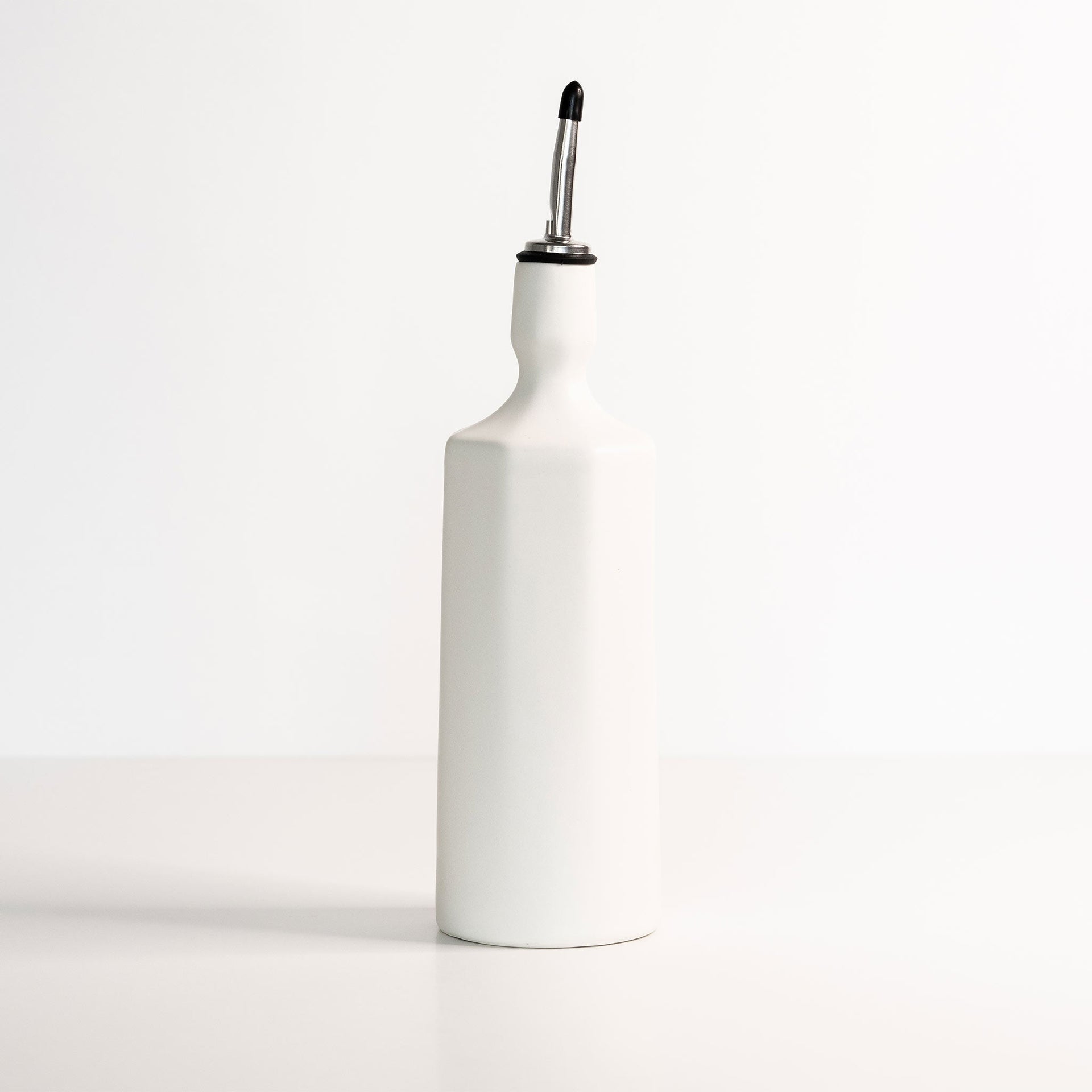 White porcelain olive oil dispenser bottle with a stainless steel pouring spout on a neutral background.