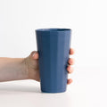 A hand holding a minimalist blue matte porcelain pint cup against a white background
