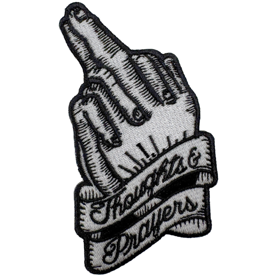 Close up of a black and white iron-on patch featuring an engraved style hand with fingers crossed.