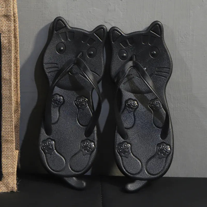 A pair of black and a pair of gold cat-shaped flip flops displayed against a dark background.