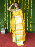Woman wearing a yellow soft handloom silk saree with intricate gold zari woven borders and matching blouse.