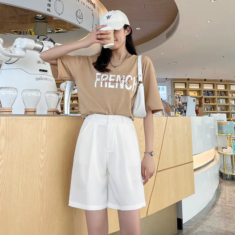 A woman wearing crisp white high waist wide leg shorts paired with a tan t-shirt in a bright cafe setting