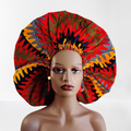 A person wearing a large, vibrant, reversible African print bonnet with a protective silk lining.