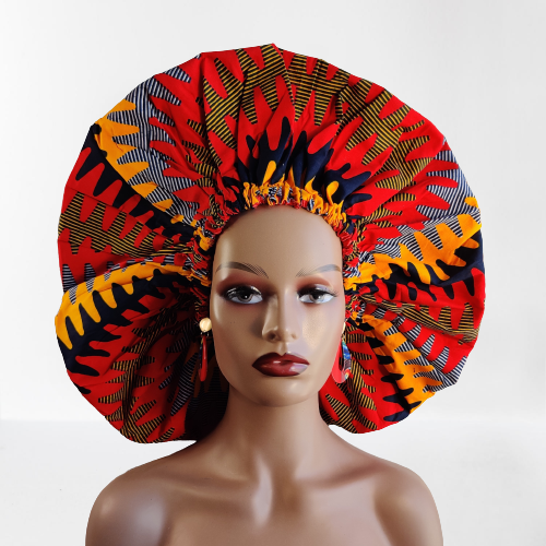 A person wearing a large, vibrant, reversible African print bonnet with a protective silk lining.
