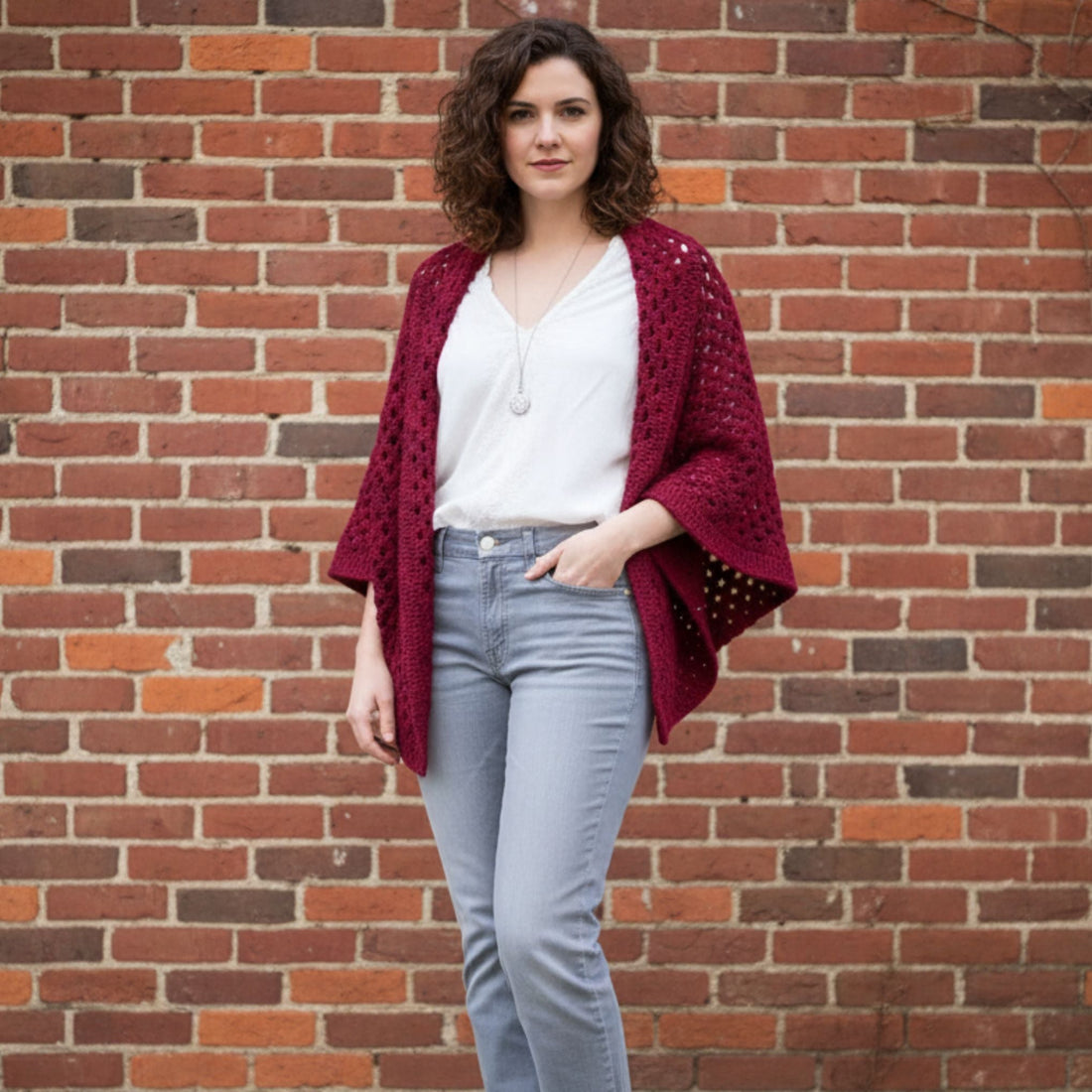 A close-up of a maroon and burgundy granny square crochet cardigan with three-quarter sleeves in a boho style.