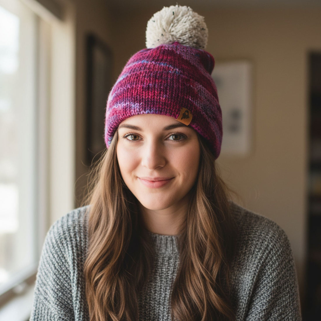 Close up of a hand-knitted burgundy and purple double brim hat with a cream speckled pom-pom.