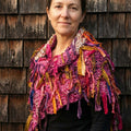 Colorful fringe knit scarf in pink, magenta, purple, and mustard yellow draped over a shoulder
