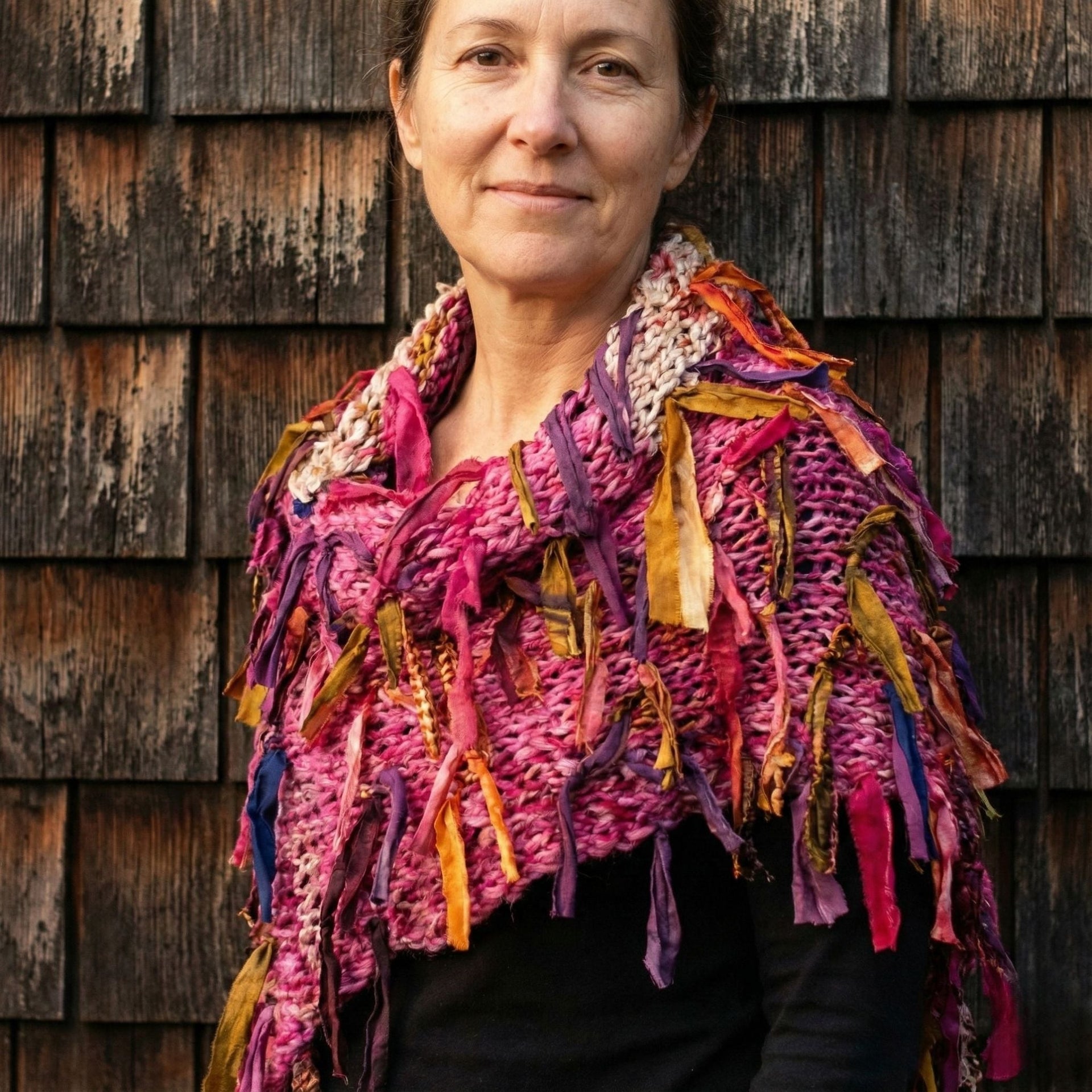 Colorful fringe knit scarf in pink, magenta, purple, and mustard yellow draped over a shoulder
