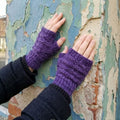 Close up of deep purple heathered knit fingerless mitts on a person's hands in a cozy winter setting.