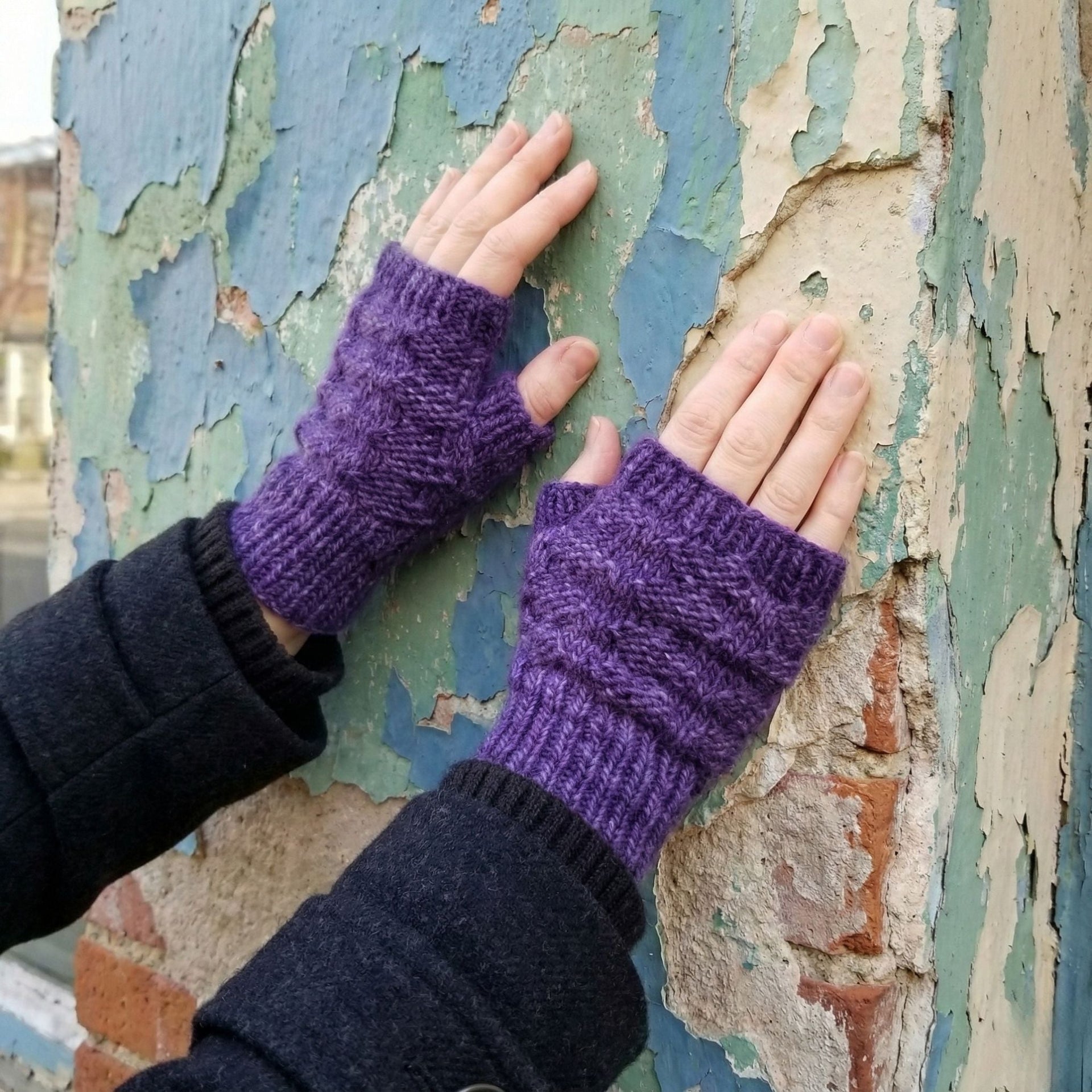 Close up of deep purple heathered knit fingerless mitts on a person's hands in a cozy winter setting.