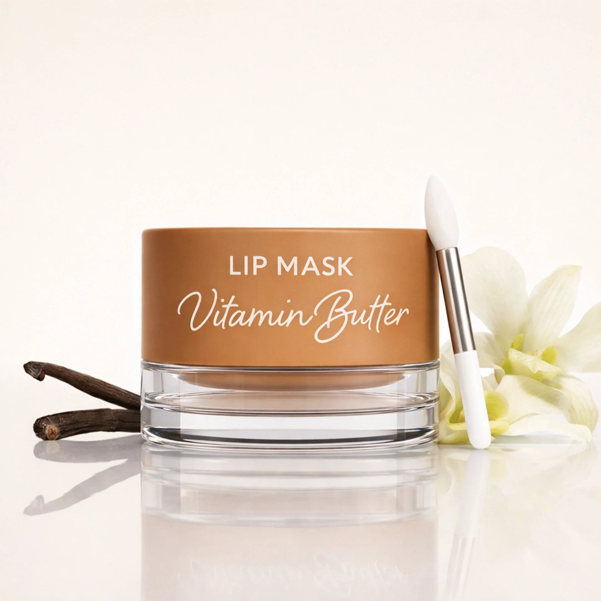 Jar of Vanilla Vitamin Butter lip mask with an applicator brush next to vanilla beans