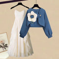A two-piece set consisting of a blue cropped long-sleeve jacket with a white flower detail and a white spaghetti strap midi dress.