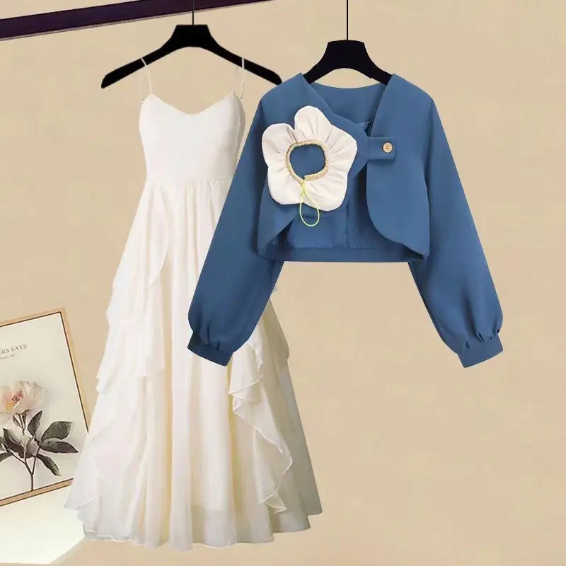 A two-piece set consisting of a blue cropped long-sleeve jacket with a white flower detail and a white spaghetti strap midi dress.