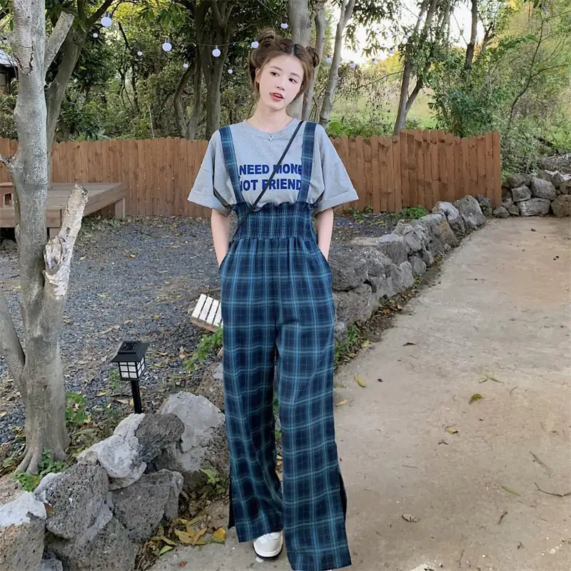 A woman wearing plaid wide-leg overalls with a smocked waist and side slits over a grey t-shirt.
