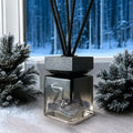 Limited edition Winter's Eve reed diffuser in a glass bottle with black reeds and crystals, set against a snowy pine backdrop.