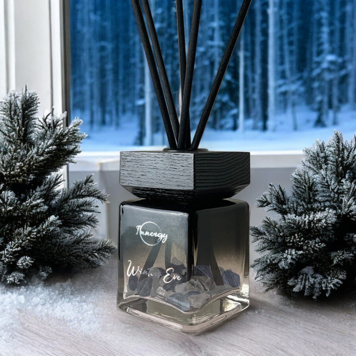 Limited edition Winter's Eve reed diffuser in a glass bottle with black reeds and crystals, set against a snowy pine backdrop.