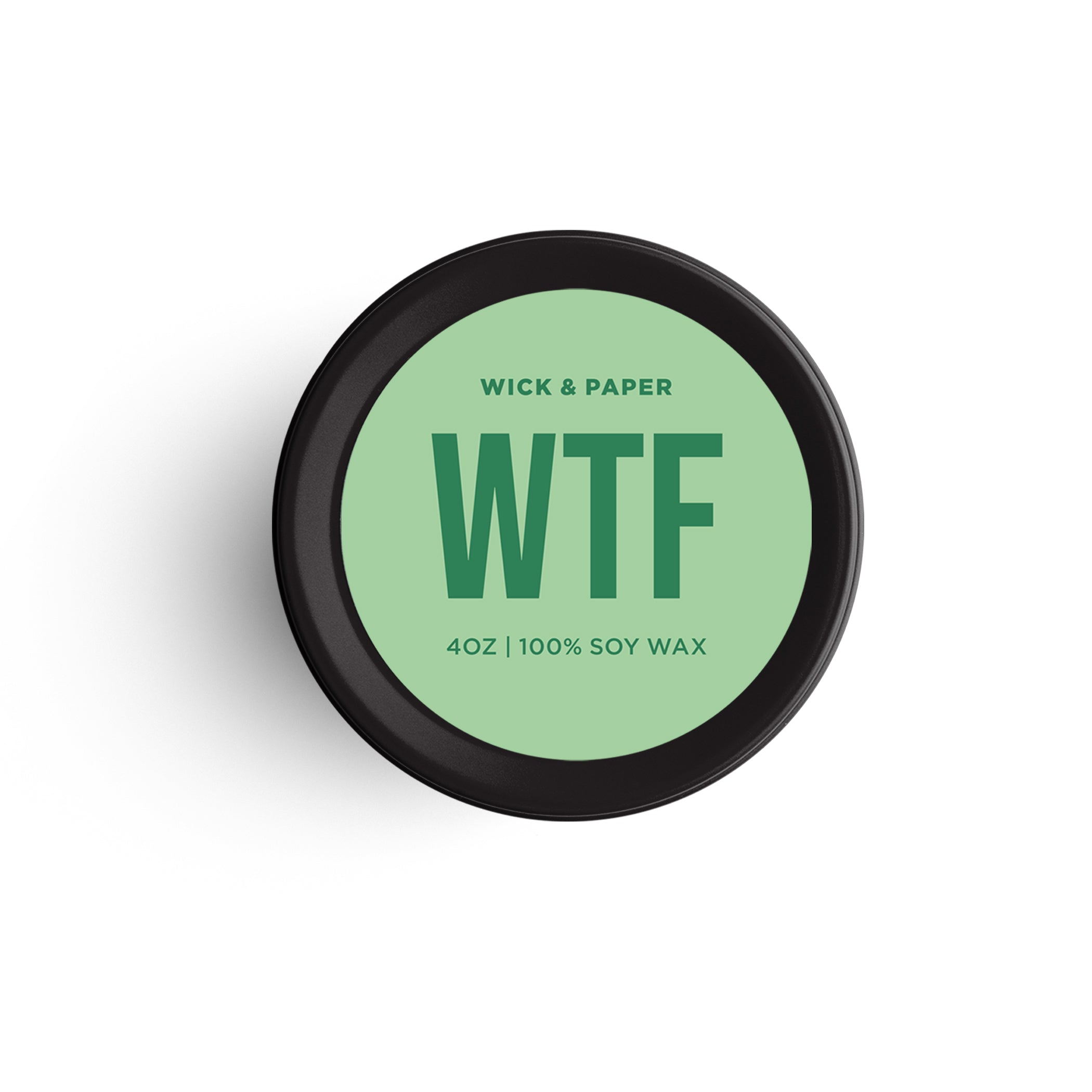 A 4oz black tin candle labeled WTF with a green sticker, surrounded by minimalist styling items.