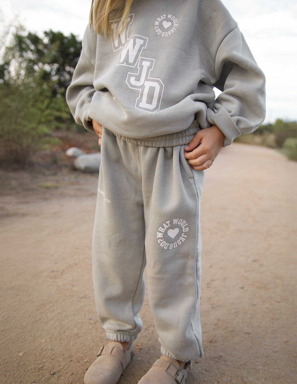 Kids wearing grey varsity sweatpants with white graphic text in a casual streetwear setting.