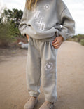Kids wearing grey varsity sweatpants with white graphic text in a casual streetwear setting.