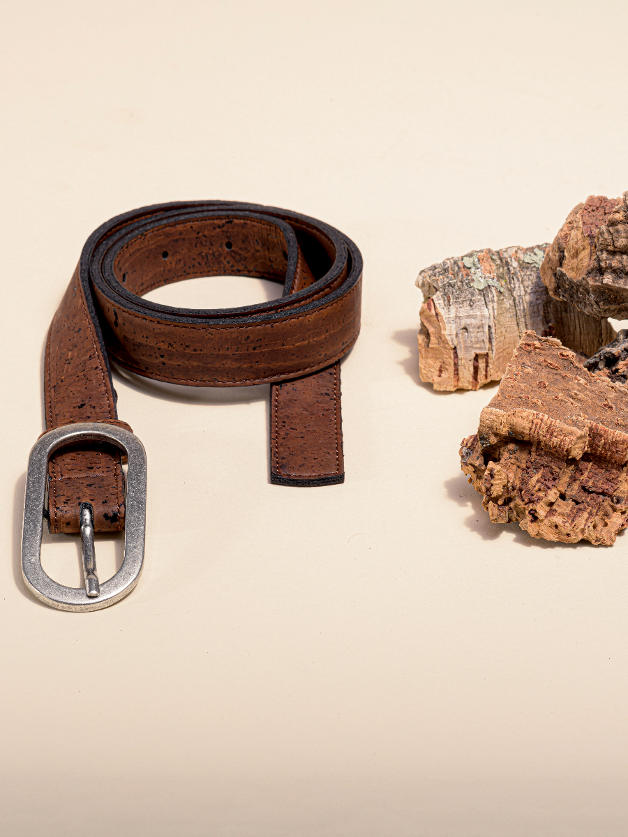 Brown women's vegan cork leather belt coiled next to raw cork bark