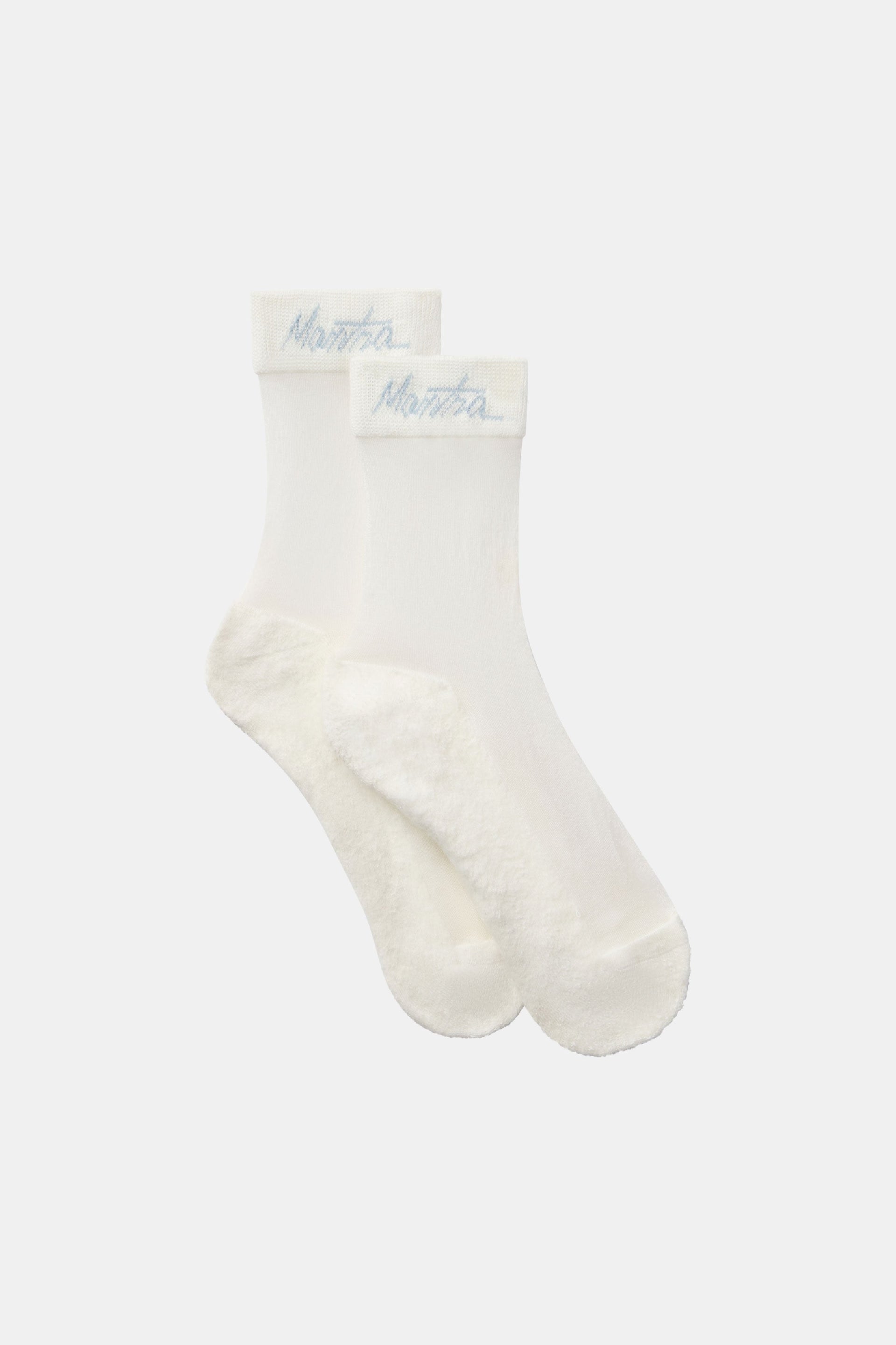 Close-up of a pair of off-white sheer golf socks with a cushioned footbed and Mantra script branding on the ribbed cuff.