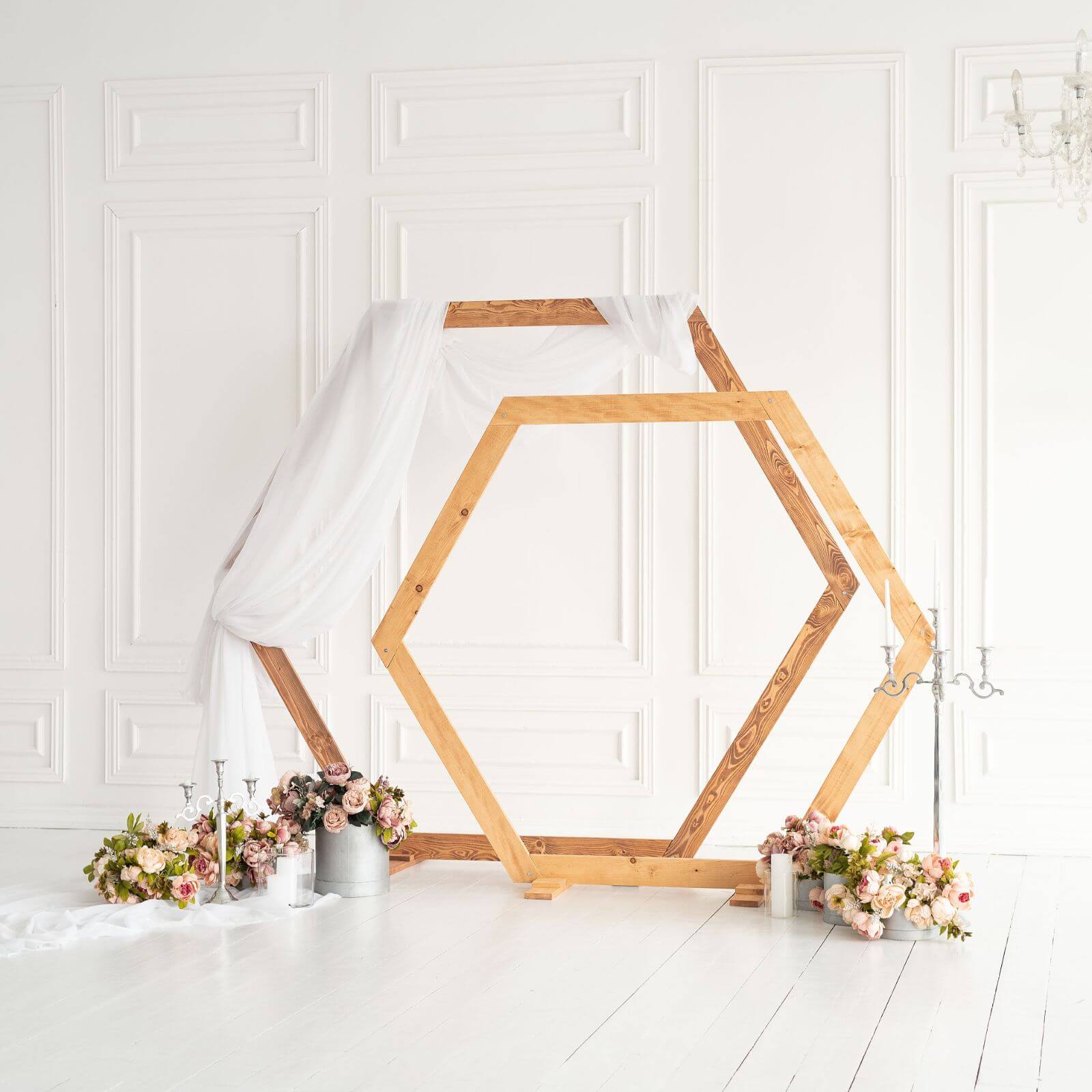 A wooden hexagon-shaped wedding arch standing as a ceremony backdrop in an indoor venue