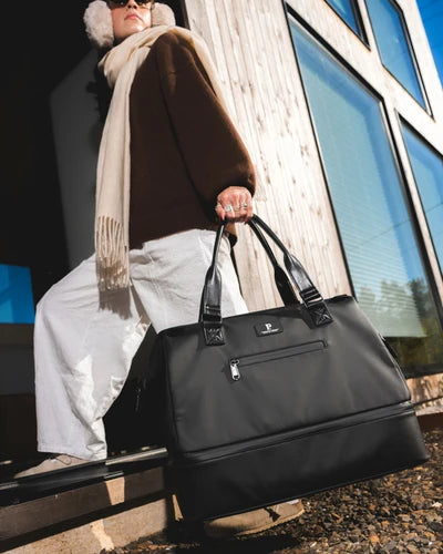 Person holding a black handbag in front of a building with large windows.