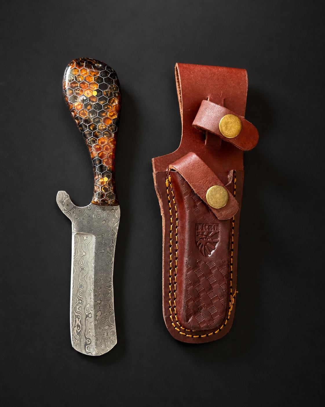 Titan Amber Hive Damascus bull cowboy cutter with honeycomb resin handle and leather sheath on a wooden office desk