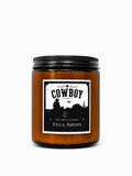 A rustic Cowboy themed soy wax candle in a dark glass jar, styled for western or lodge home decor.