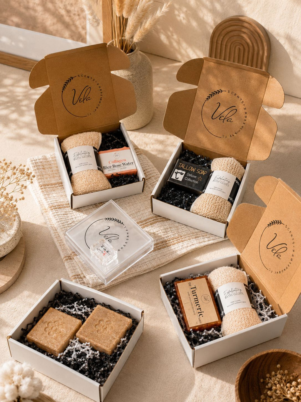 A curated set of Vela artisan soaps in neutral kraft paper packaging with black paper fill and a bath glove.