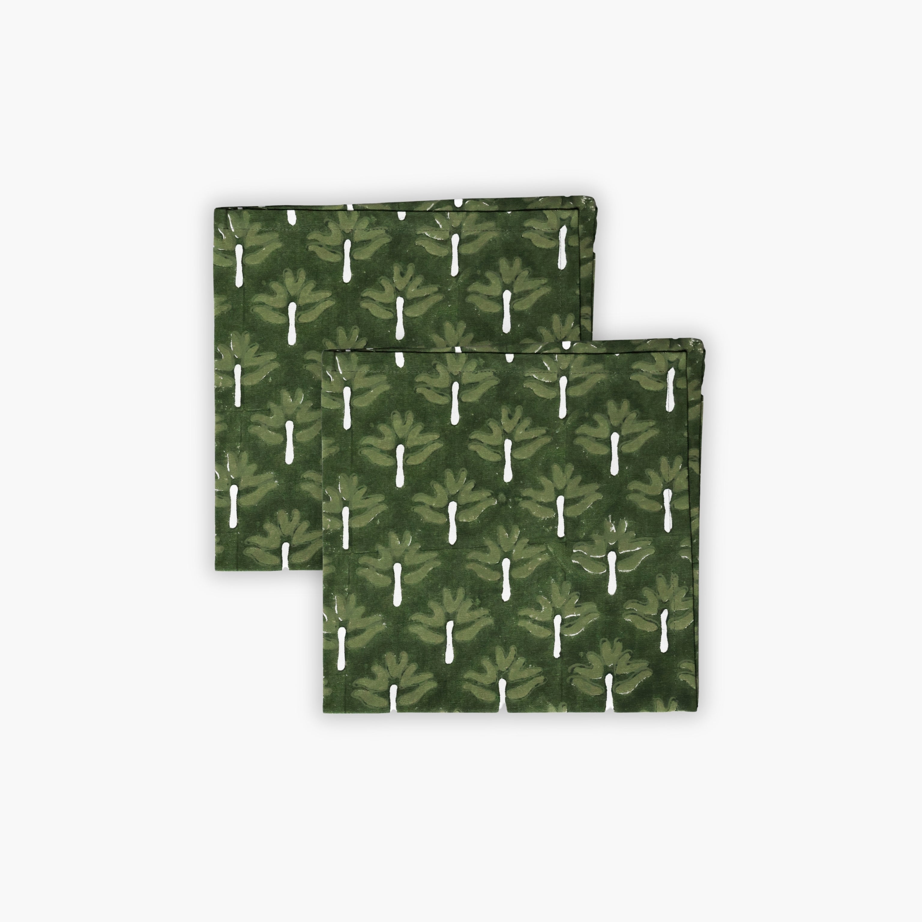 Set of two Zeenat chive green cotton table napkins with white botanical hand-block print patterns on a dining table.