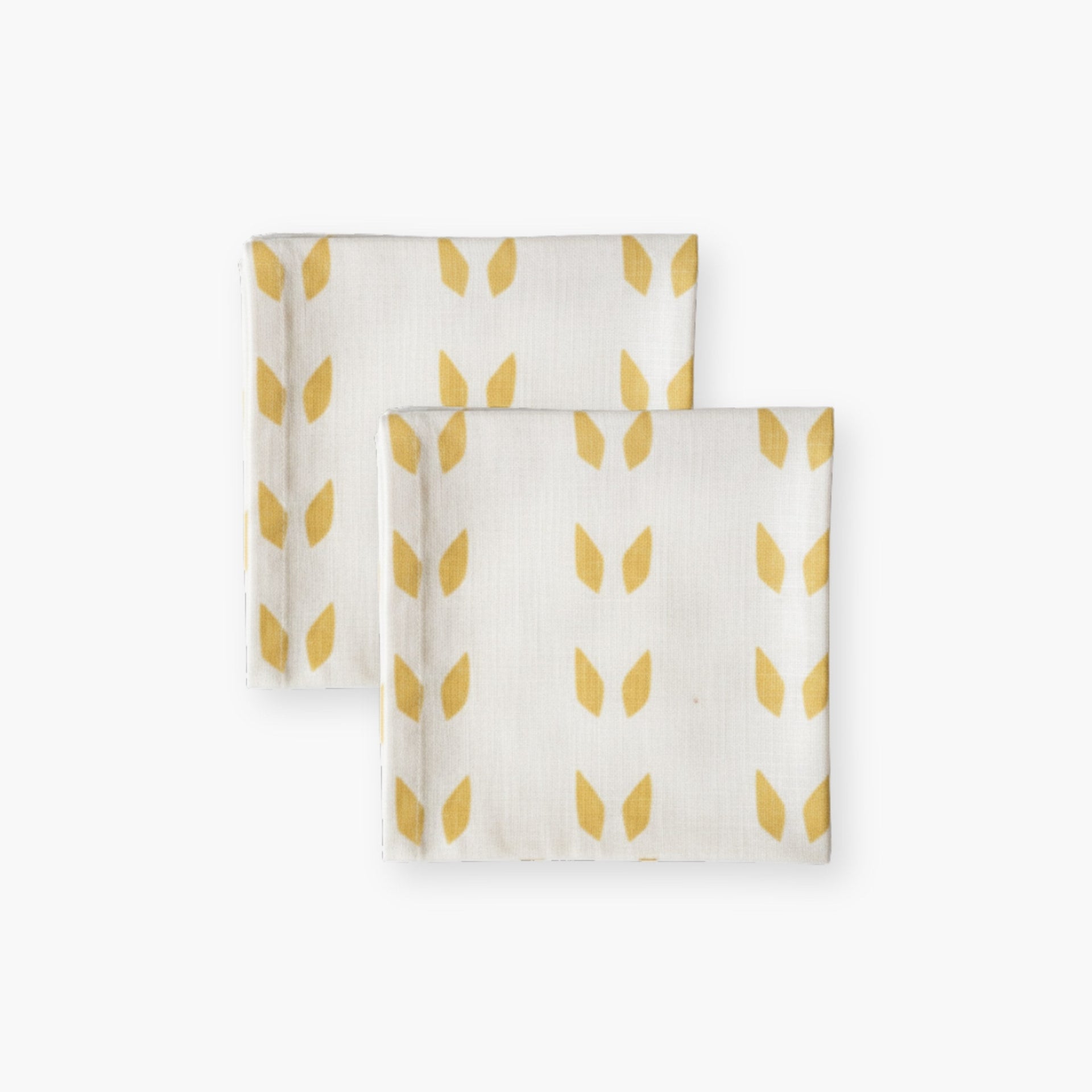 A set of two white linen table napkins with mustard terracotta geometric print, neatly folded on a wooden table.