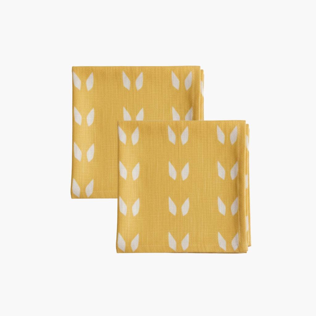 A set of two mustard and white linen table napkins featuring geometric terracotta-style patterns.