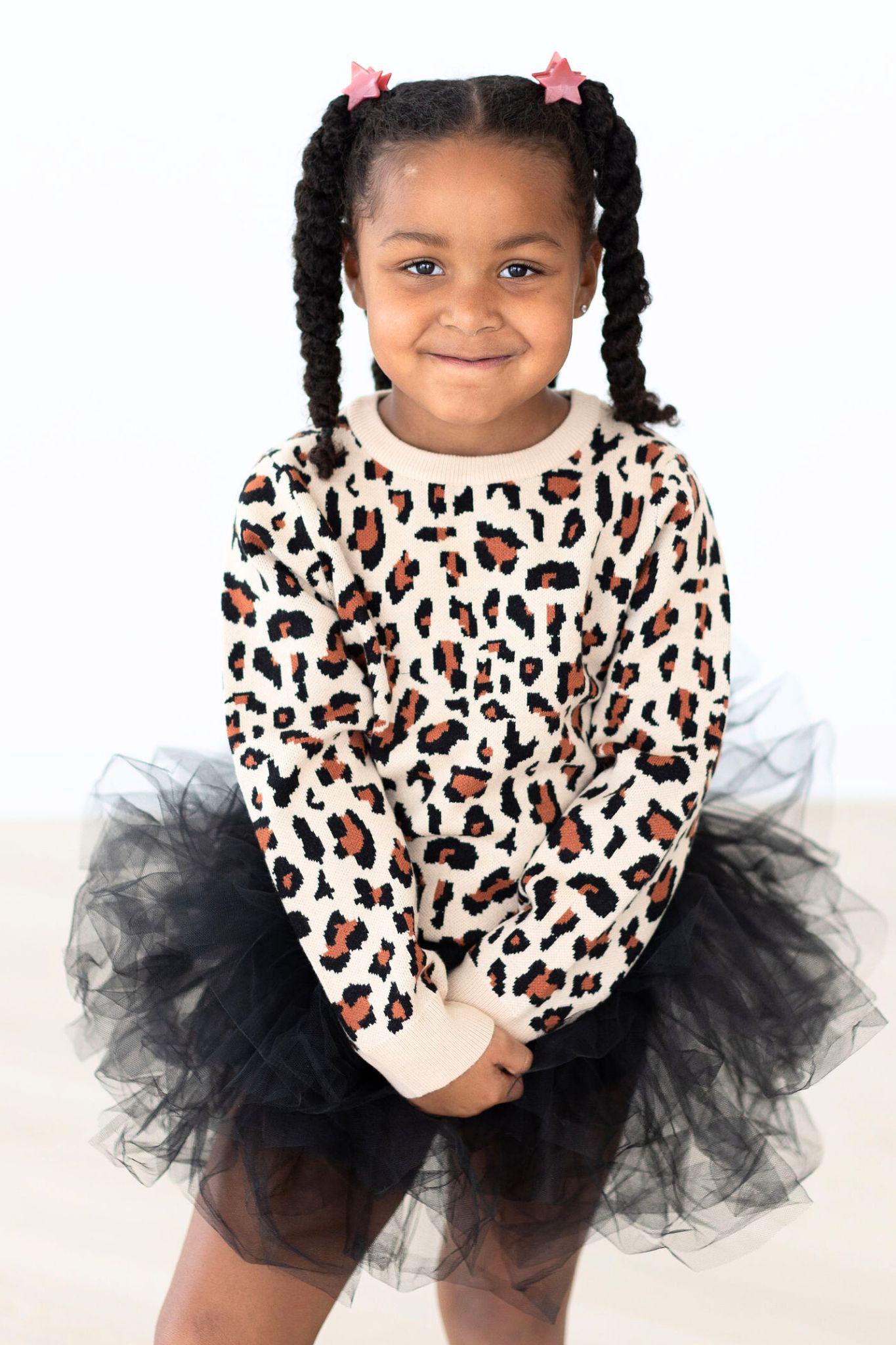 Young girl wearing a beige leopard print long sleeve sweater with a black tulle skirt