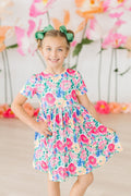 A young girl smiling wearing a bright, floral print short sleeve twirl dress with pockets.