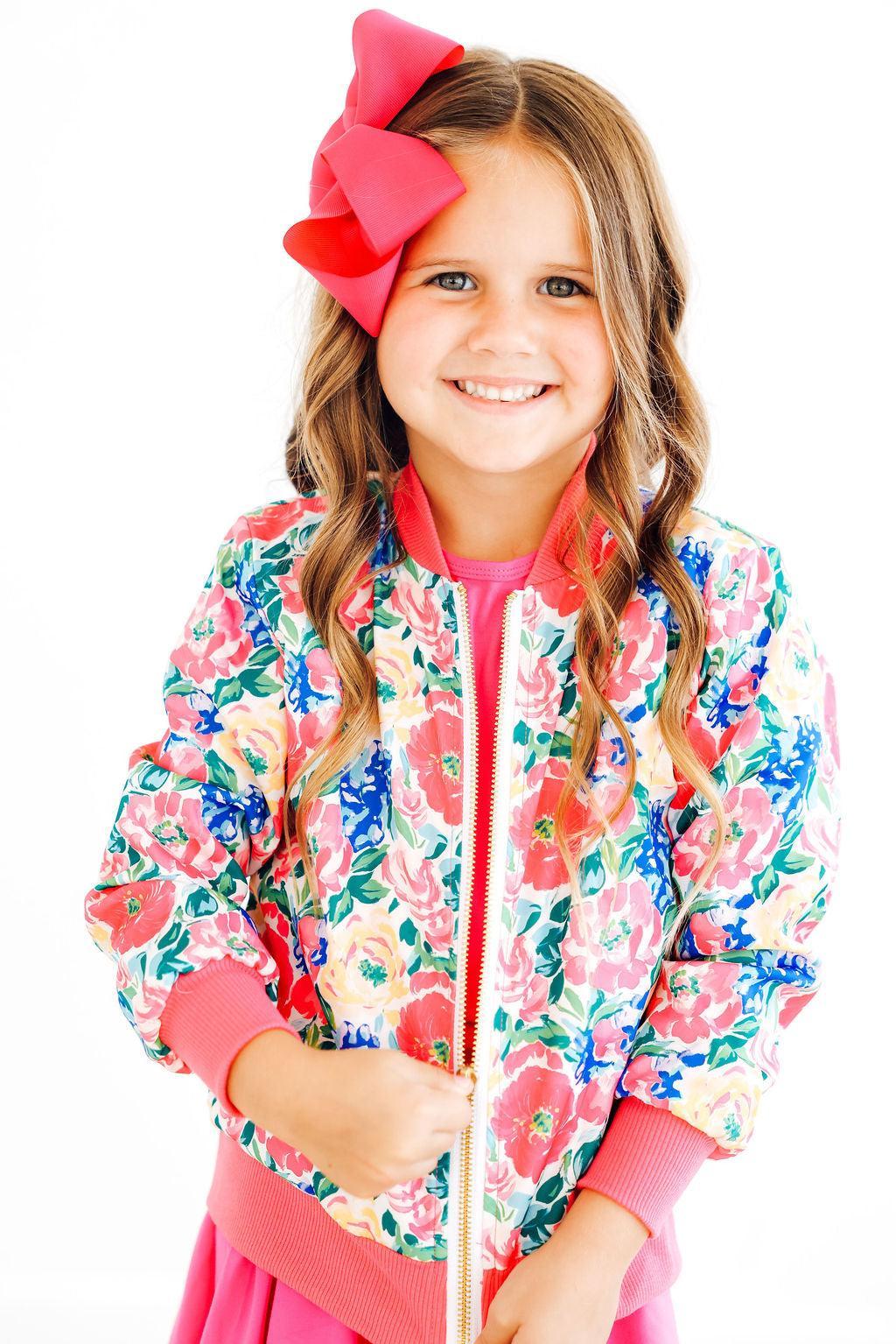 Young girl wearing a colorful floral print satin bomber jacket with ribbed pink trim.