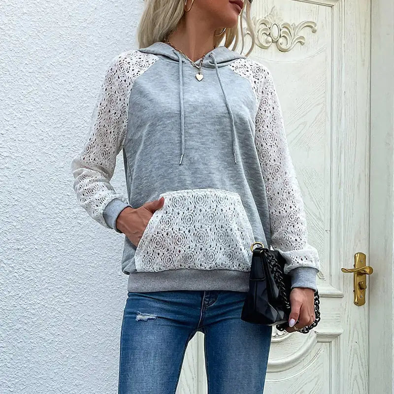 A woman wearing a grey long sleeve sweatshirt with white lace detailing on the sleeves and a matching lace front pocket.