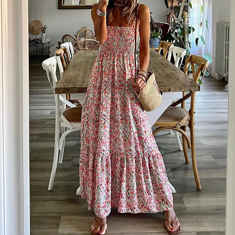 A woman wearing a pink floral printed sleeveless midi suspender dress with a smocked bodice and tiered skirt.