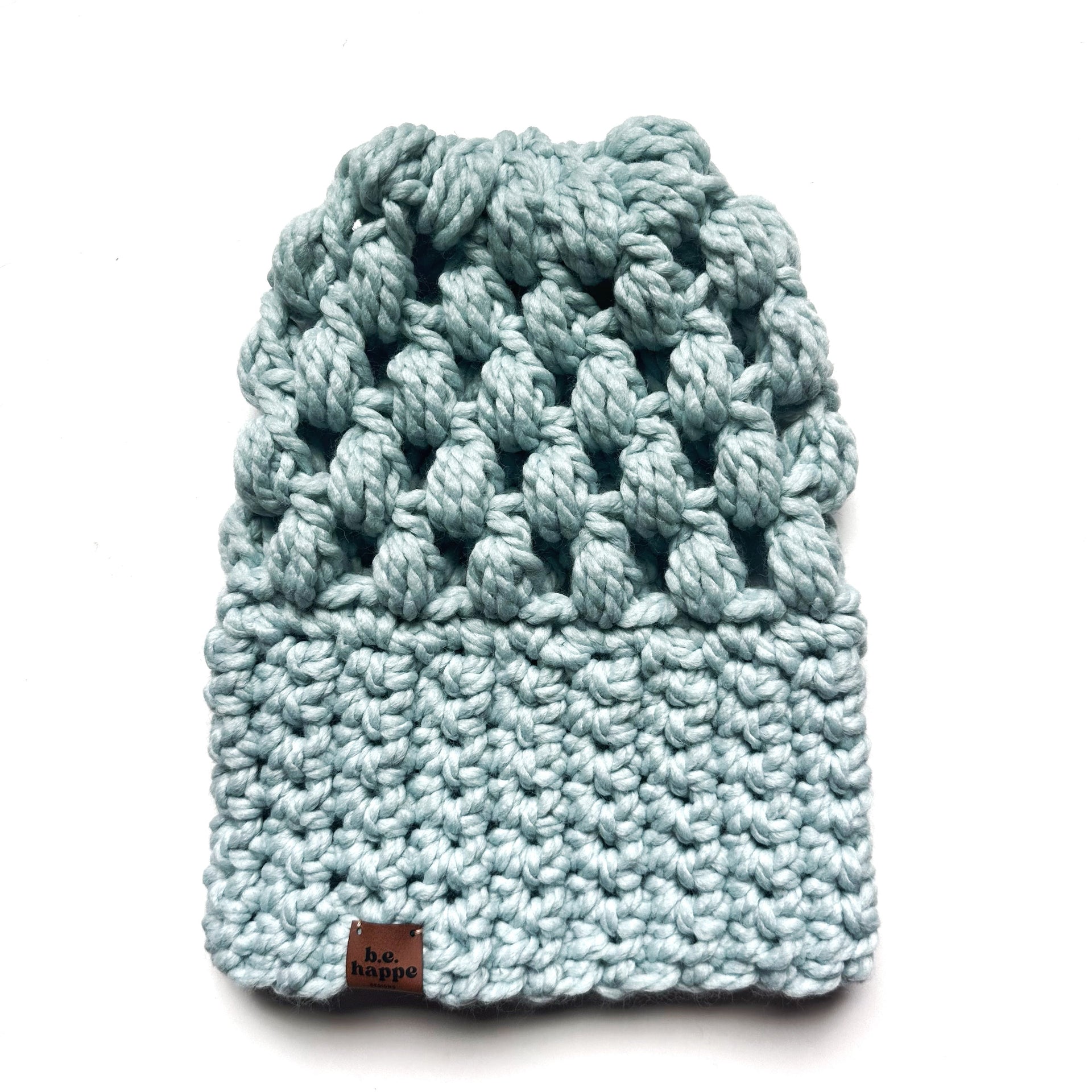 A light blue crochet slouchy beanie hat resting on a white background, featuring a chunky knit design and a branded leather tag.