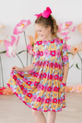 Young girl wearing a bright floral print 3/4 sleeve dress with side pockets and a full, twirl-worthy skirt.