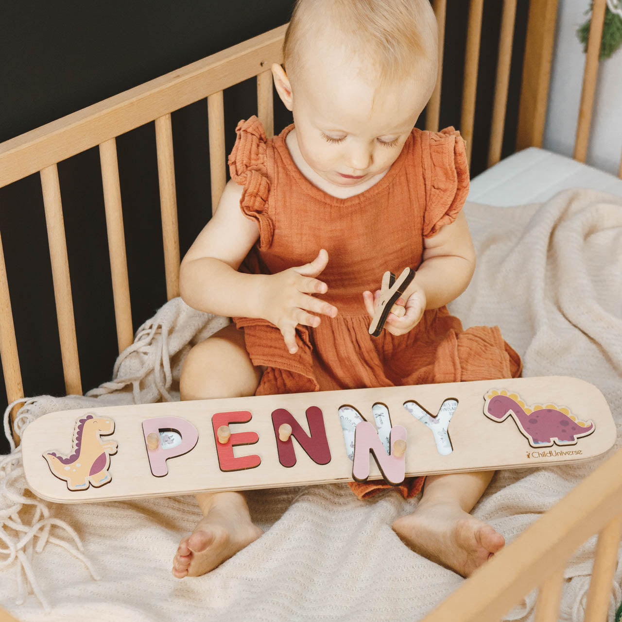 Personalized wooden dinosaur name puzzle for girls in pastel colors on a minimalist nursery shelf.