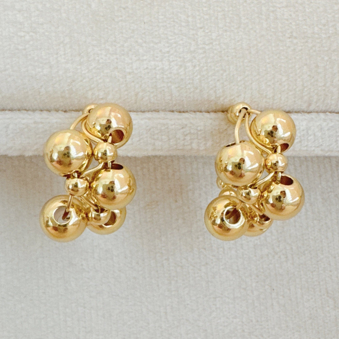 A pair of gold-toned woven bubble design hoop earrings displayed on a velvet jewelry stand and modeled on a person.
