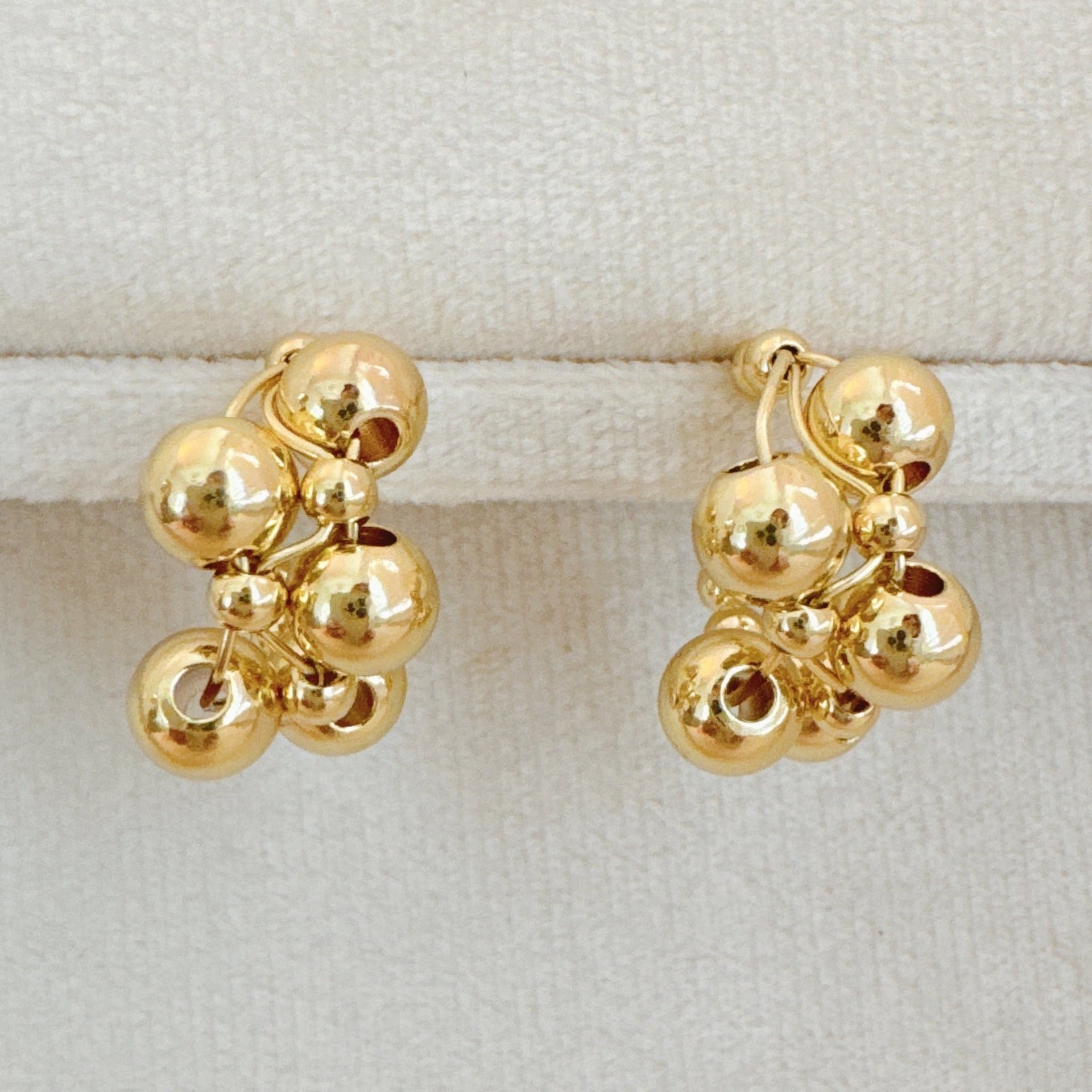 A pair of gold-toned woven bubble design hoop earrings displayed on a velvet jewelry stand and modeled on a person.