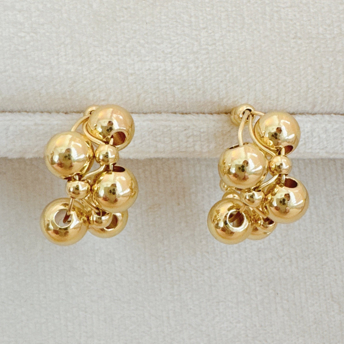 A pair of gold-toned woven bubble design hoop earrings displayed on a velvet jewelry stand and modeled on a person.