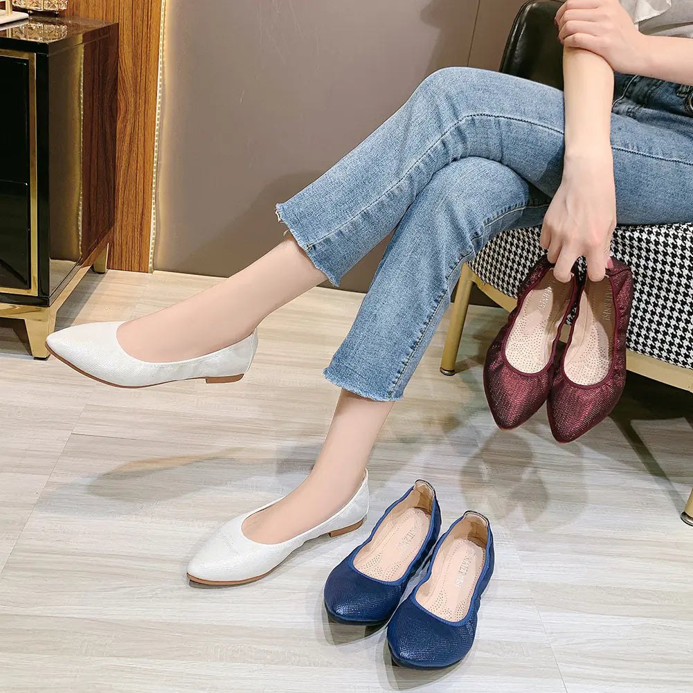 A pair of pointed toe flat shoes with a textured gold shimmer finish shown on a model's feet.