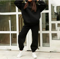 A woman wearing a matching gray plush hooded sweatshirt and jogger pants set outdoors.